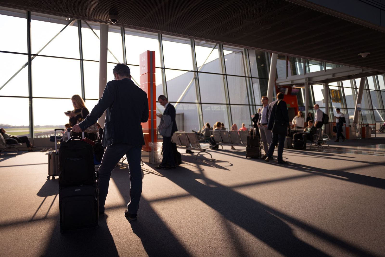 Travellers with luggage crossing a sunlit airport terminal