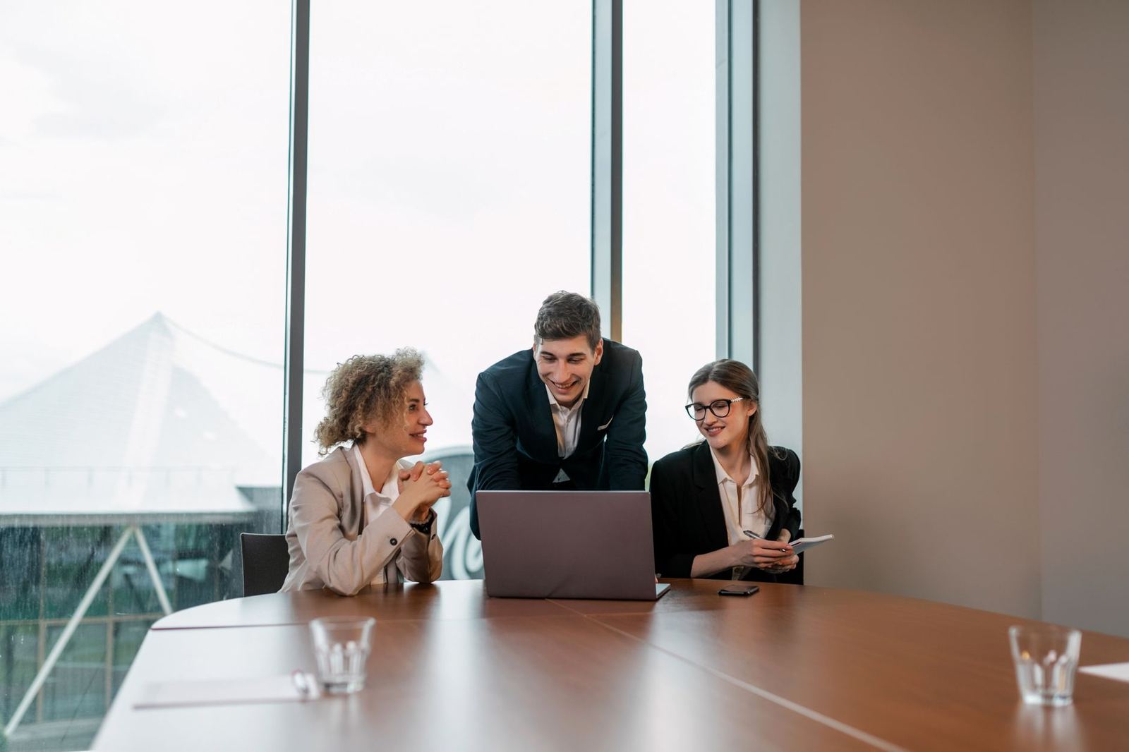 Three colleagues reviewing a schedule on a laptop in a glass-walled office